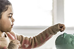 young girl putting coins into her piggy bank