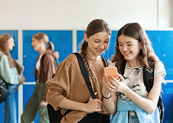 two teens looking at a phone in school hallway
