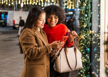 women looking at phone outside store window