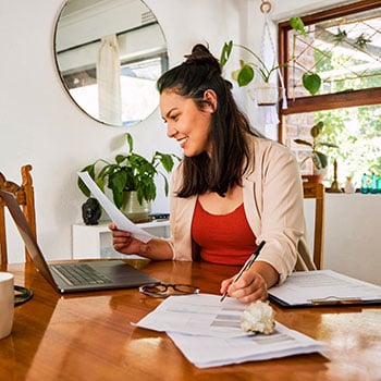 Young woman doing paperwork and using laptop computer