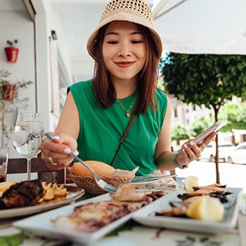 Young woman eating at restaurant and holding mobile phone